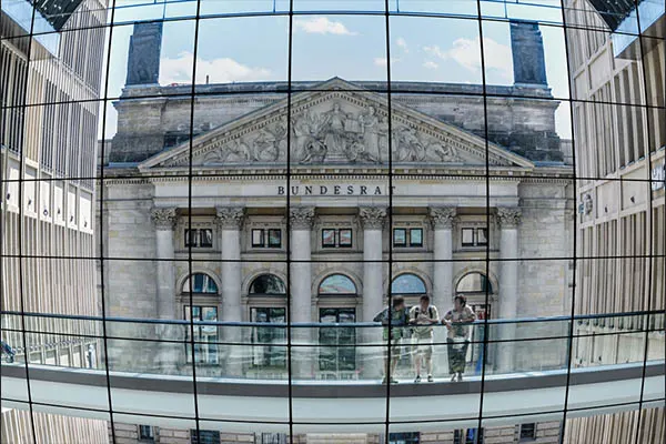 Distorted reflection of the Bundesrat building and people on a bridge in a curved glass facade, ideal for standardized camera testing