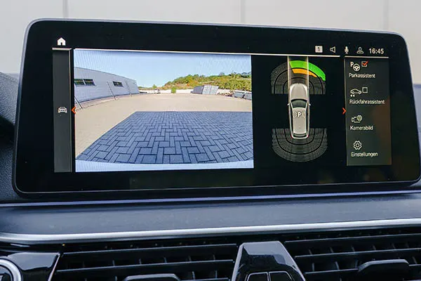 Car dashboard screen showing a parking assist display with camera view, proximity sensors, and German menu options