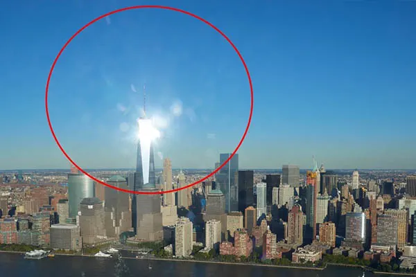 Bright sun flares over a skyscraper in a city skyline, highlighted by a red circle, for standardized camera testing
