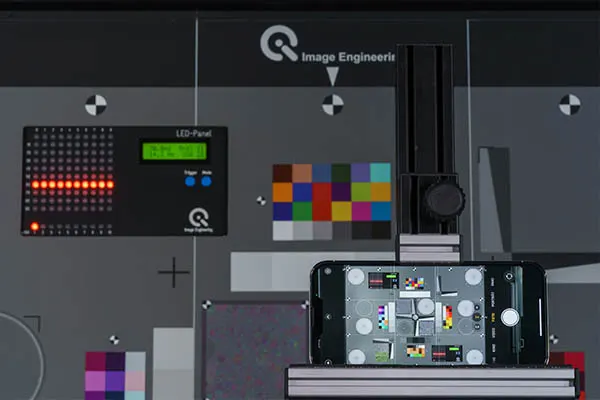 A smartphone mounted for standardized camera testing, displaying a live view of the test chart with color and gray scales