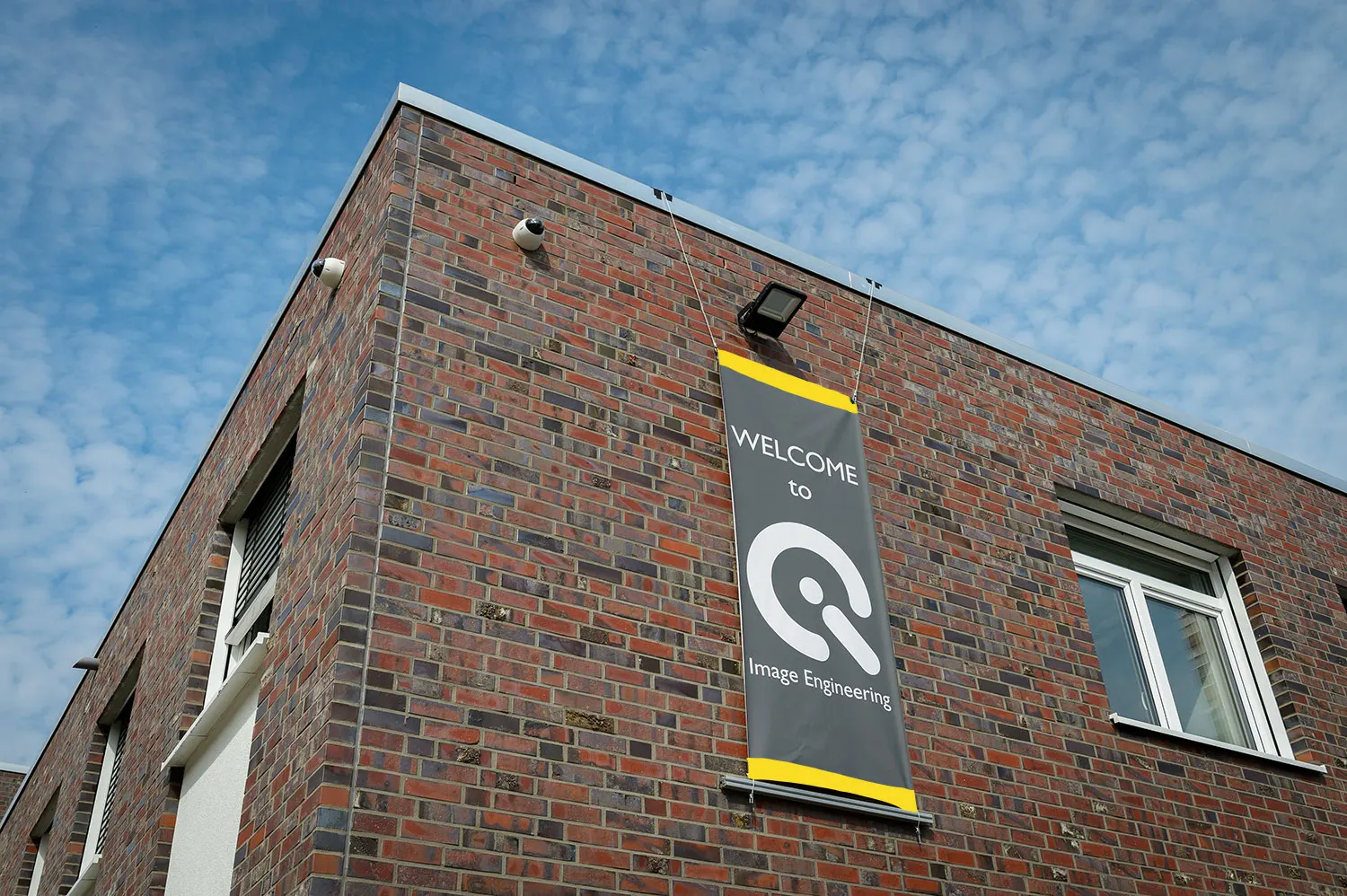 Exterior view of a brick building with a "Welcome to Image Engineering" banner hanging under a clear sky