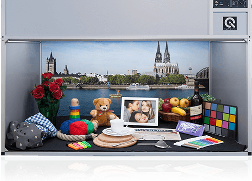 A light booth showcasing various objects, a color checker, and a backdrop of the Cologne Cathedral